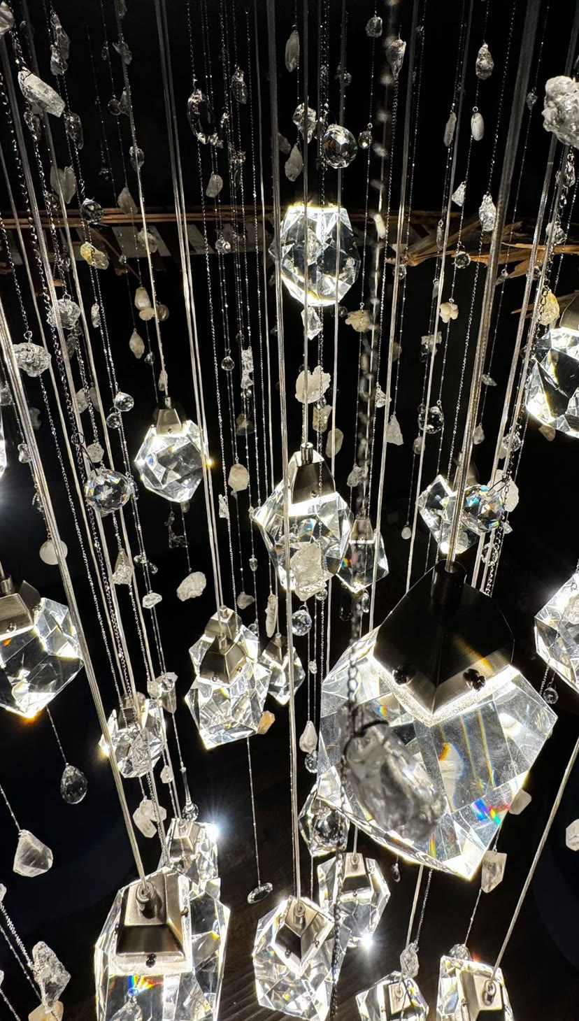 Looking up into the cascade: large faceted crystal pendants lit from within, surrounded by strands of rough quartz and small crystal beads.