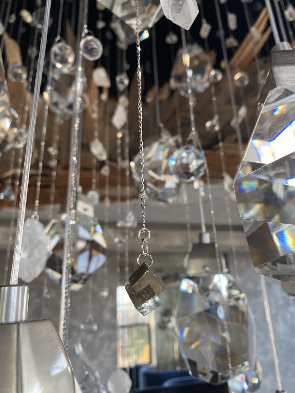A small pyrite cube hanging on a fine silver chain among clear crystals throwing rainbow refractions, the wood lath opening above.